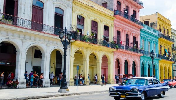 Farbige Häuser in Kuba mit einem blauen Auto welches auf der Strasse fährt