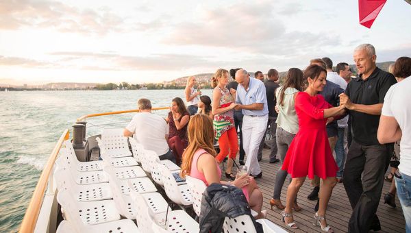 Schiff auf dem See mit tanzenden Paaren auf dem Deck mit guter Stimmung und lachenen Gesichetern