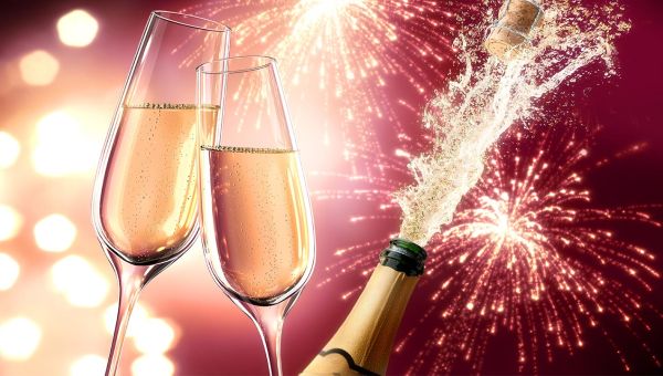 Zwei Gläser stossen an Neujahr an im Hintergrund eine Champagnerflasche und Feuerwerk