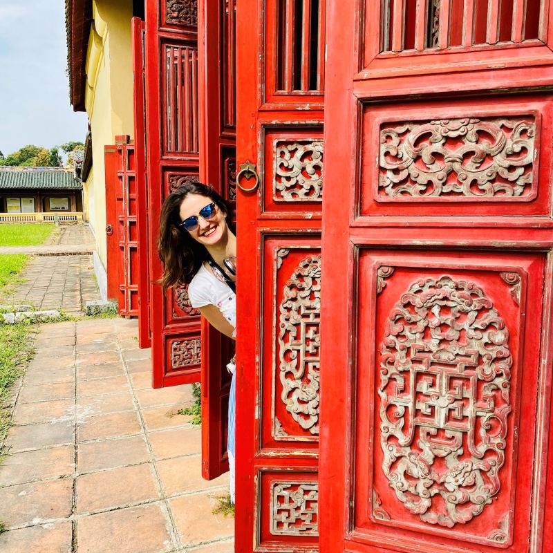 Frau schaut hinter einer roten asiatisch Türe hervor die zu einem Tempel gehört