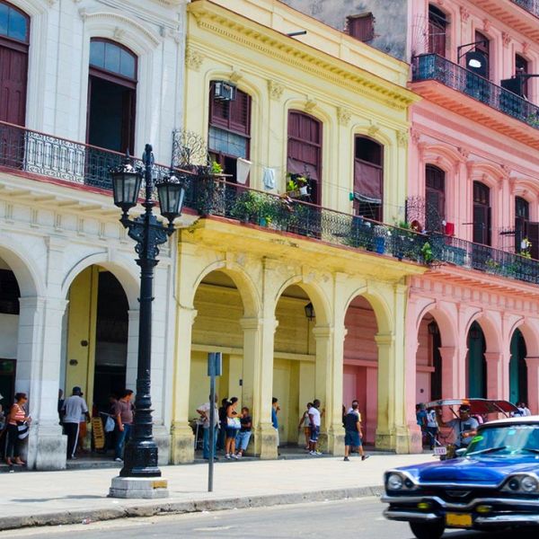Farbige Häuser in Kuba mit einem blauen Auto welches auf der Strasse fährt