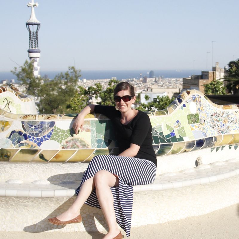 Frau sitzt mit einem Rock und schwarzen Oberteil auf einer Stein Bank in Barcelona