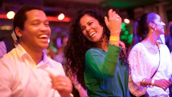 Frau im grünen Klein strahlt und lächelt beim Salsatanzen Mann im weissen Hemd lacht und tanzt neben ihr