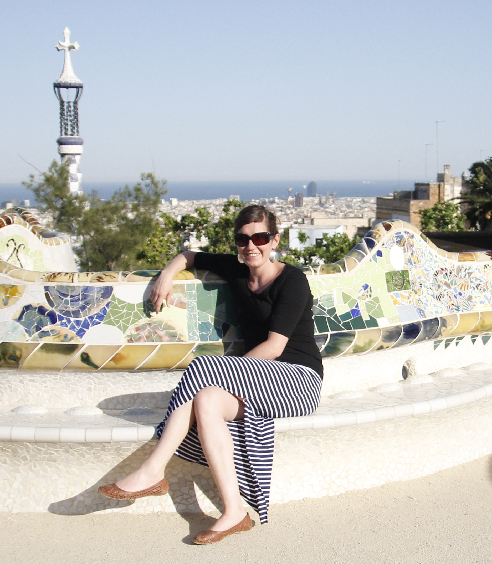 Frau sitzt mit einem Rock und schwarzen Oberteil auf einer Stein Bank in Barcelona